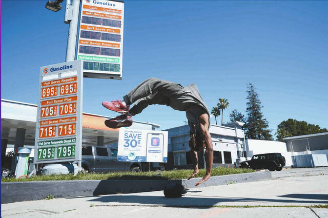 Marcus Hopkins, a street performer, does a backflip in front of advertised gas prices Monday, March 9, 2026, in Los Angeles. (AP Photo/Damian Dovarganes)