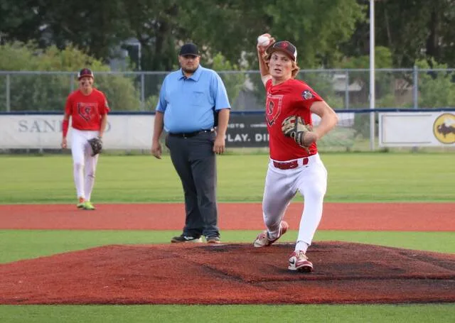 Will Heilman heaves a pitch as the umpire and second baseman Max Palmer look on during the Storms region tournament opener against Wahpeton at Starion Bank Field.
                                 Photo by Mojo Hill